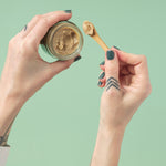 Scooping Zeeyo gut-safe dog toothpaste from an open jar, using the included bamboo scoop 