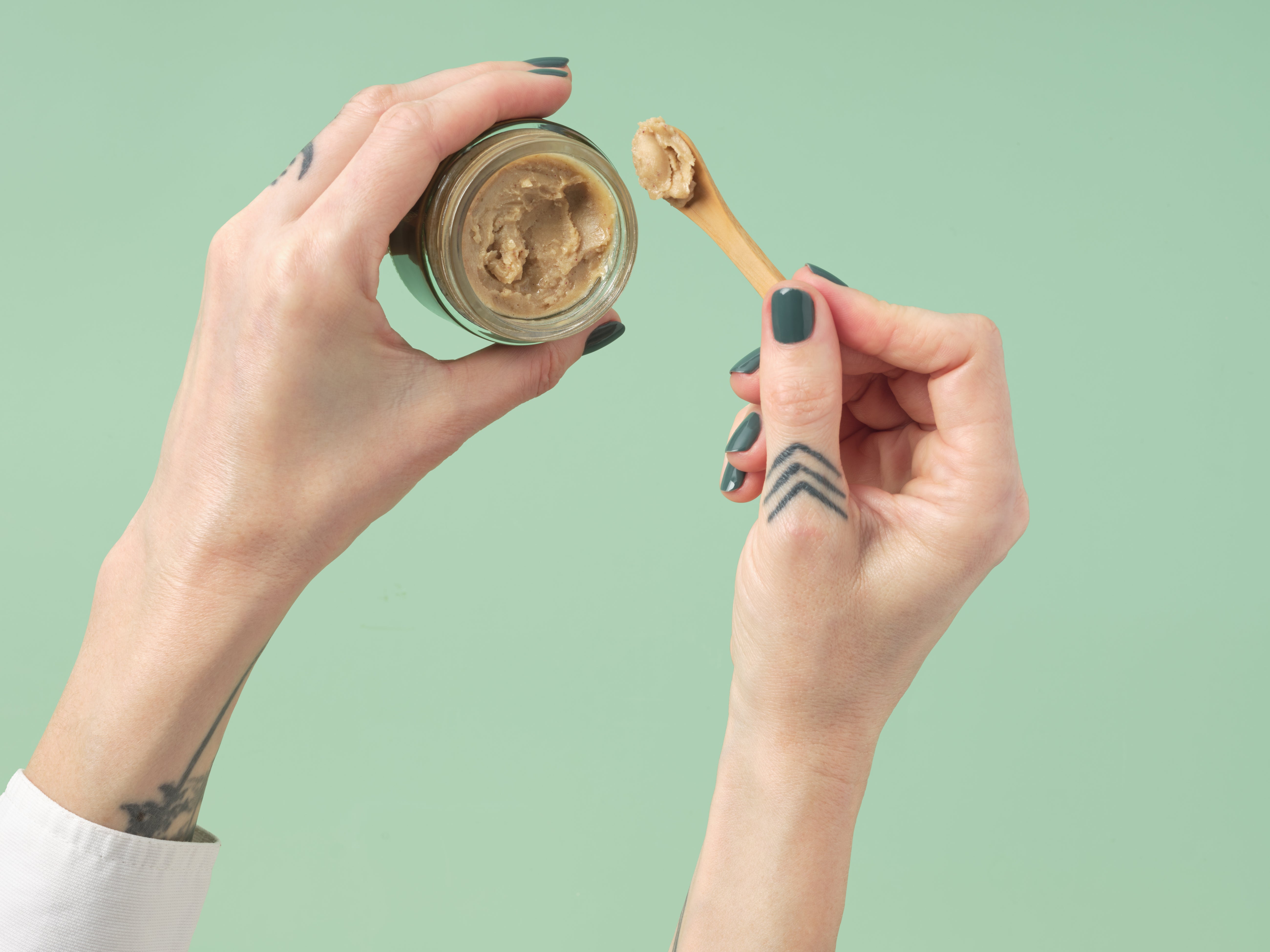 Scooping Zeeyo gut-safe dog toothpaste from an open jar, using the included bamboo scoop 
