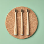 Three bamboo toothbrushes on a cork board with a green background