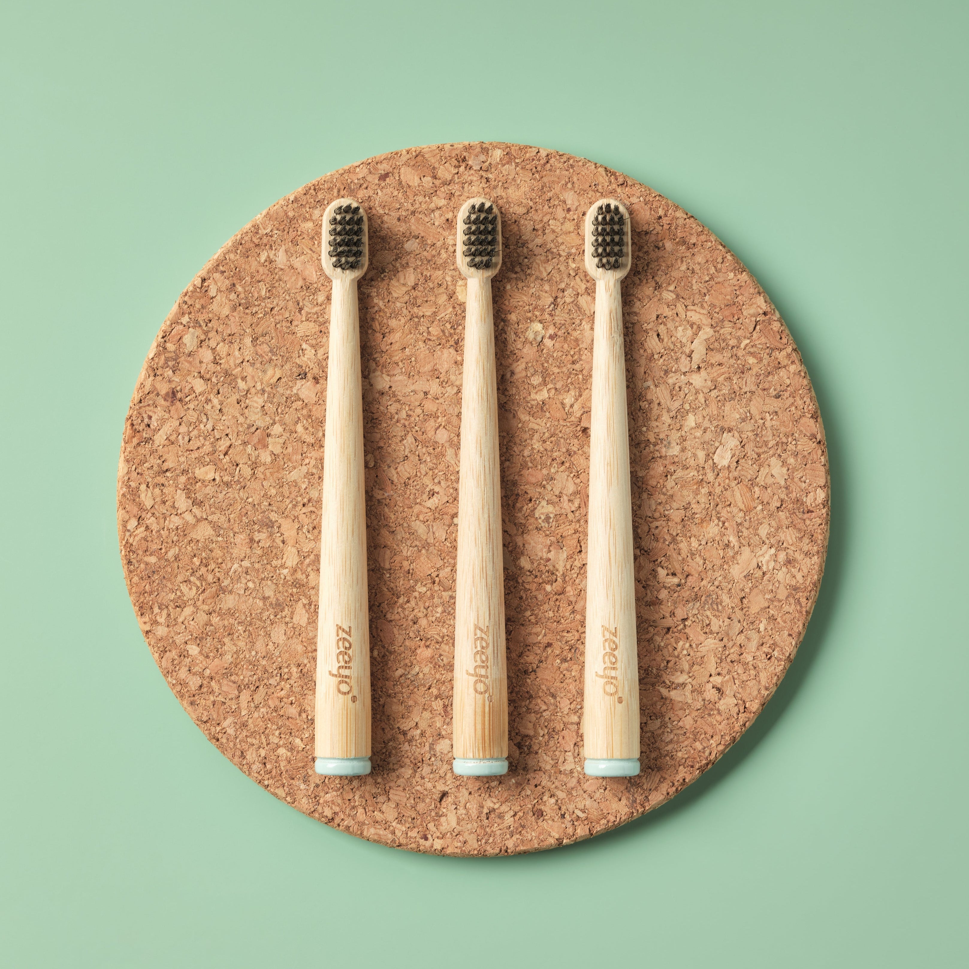 Three bamboo toothbrushes on a cork board with a green background