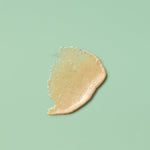 A close-up texture swatch of Zeeyo natural dog toothpaste smeared on a sage green background. The swatch reveals a thick, creamy, beige-colored paste with visible fine botanical flecks, highlighting its waterless and grit-balanced formula