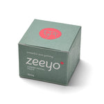 A professional studio shot of the Zeeyo Canine Dental Paste outer packaging. The box is a muted sage green with the Zeeyo logo in white and a red circular dog-line-art icon on top. The side of the box displays a clear, comprehensive list of natural, human-grade ingredients, reflecting the brand's commitment to transparency and gut-safe health